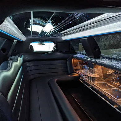 A sleek limousine interior features dark leather seating, a well-stocked bar with glasses, and a dazzling LED-lit ceiling.